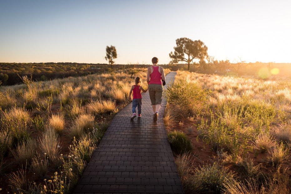 man and toddler with tank top walking on pathway between brown leaf plants during sunset